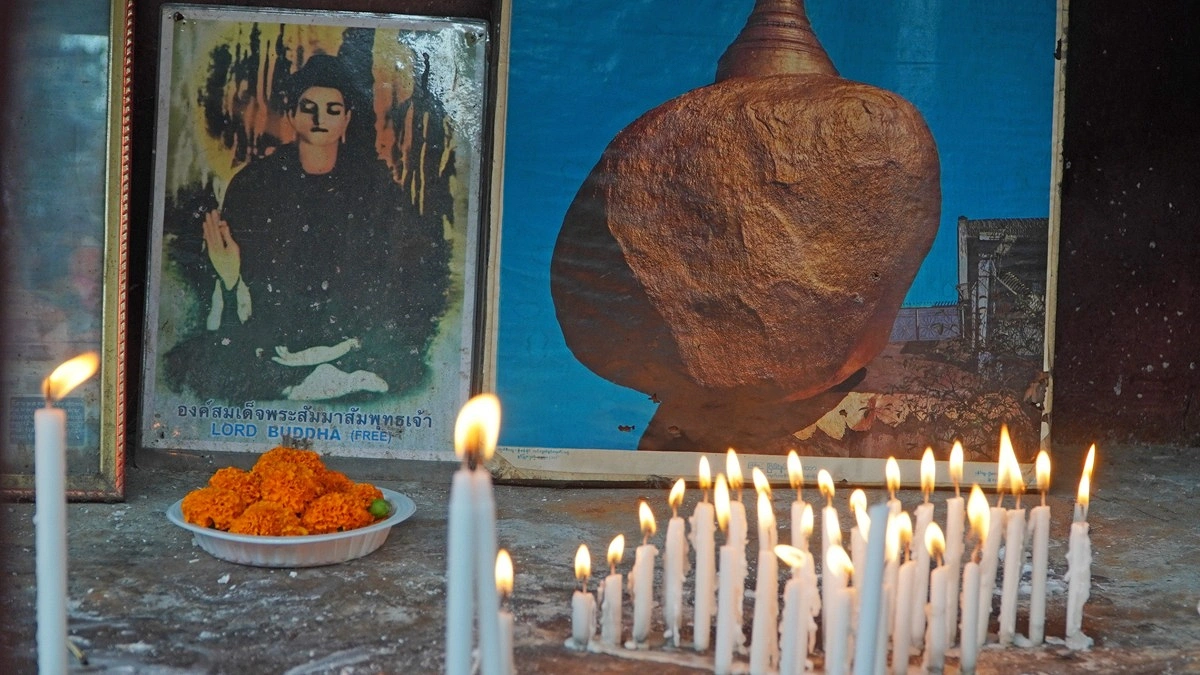 বুদ্ধের প্রতিকৃতির সামনে পাত্রে সাজিয়ে রাখা হয়েছে ফুল ও জ্বালানো মোমবাতি।