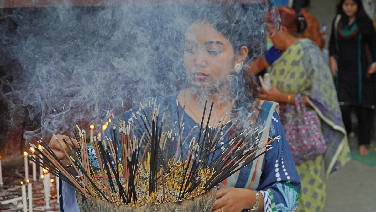 বৌদ্ধ বিহারে মোমবাতি ও ধূপকাঠি জ্বালাচ্ছেন এক পুণ্যার্থী নারী।