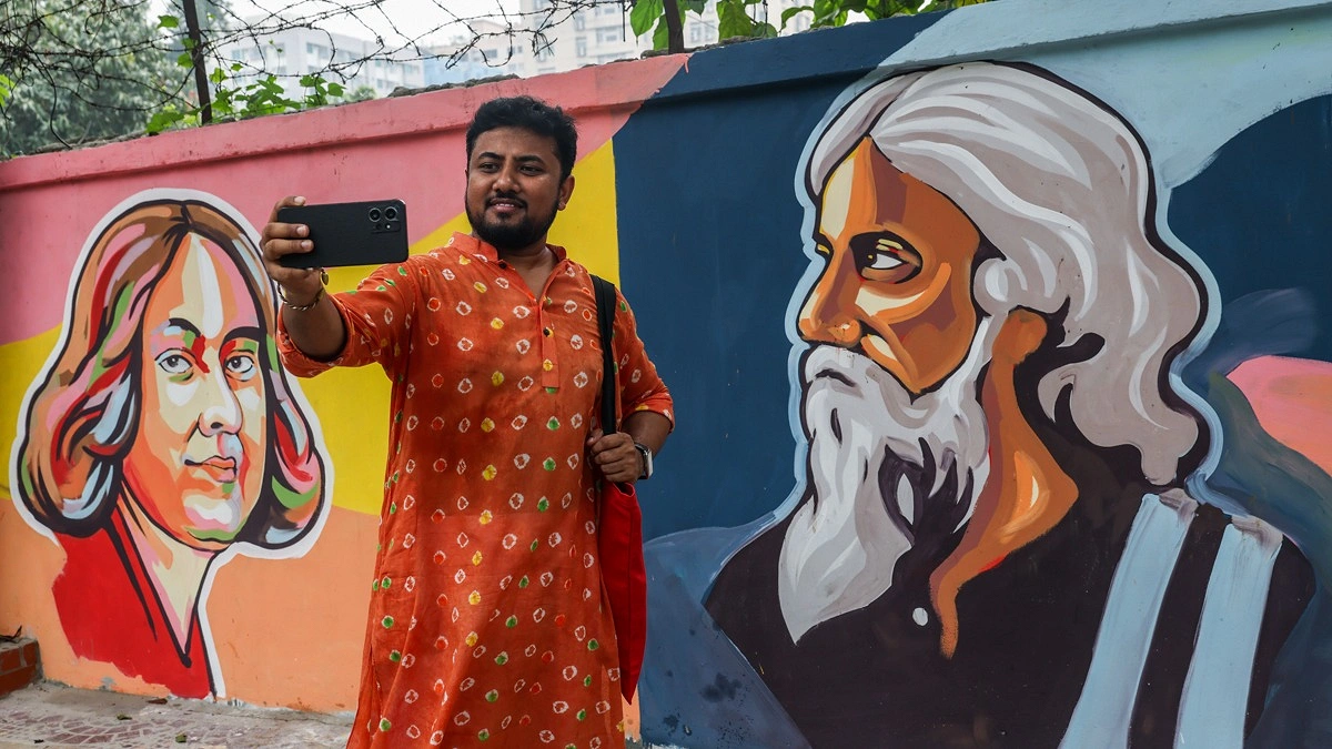 দেয়ালে আঁকা গ্রাফিতির সঙ্গে ছবি তুলছেন এক পথচারী
